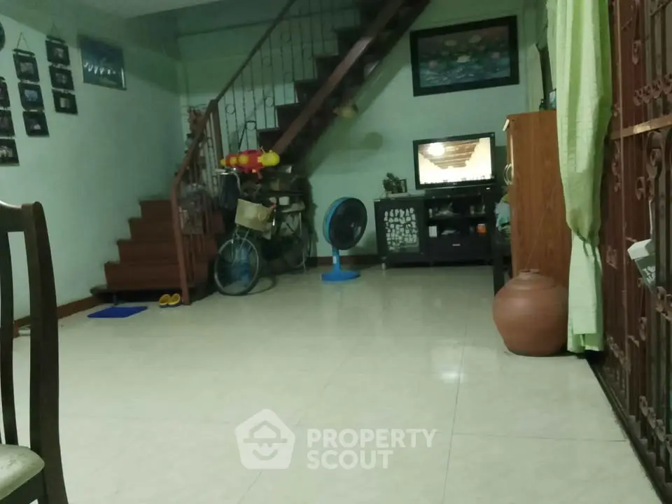 Cozy living room with staircase and tiled floor, featuring a TV and fan for comfort.