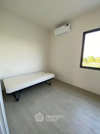 Minimalist bedroom with single bed and air conditioning, featuring a large window with natural light.