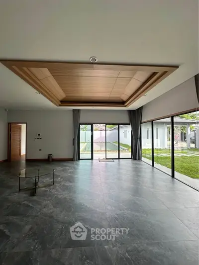 Spacious modern living room with large windows and garden view, featuring elegant ceiling design and marble flooring.