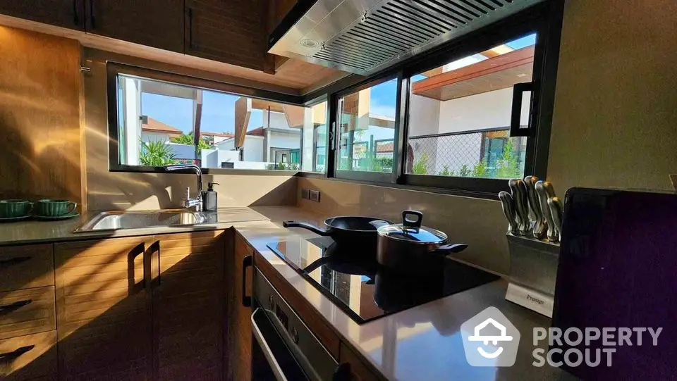 Modern kitchen with sleek countertops, induction stove, and large windows offering natural light and outdoor views.