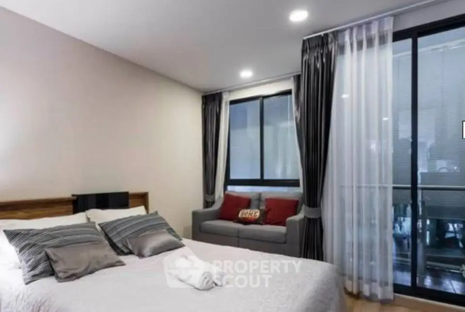 Modern bedroom with cozy bed and stylish curtains, featuring a small sofa and large windows for natural light.
