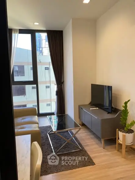 Modern living room with large window, stylish furniture, and natural light in urban apartment.