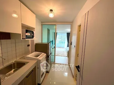 Modern apartment kitchen with washing machine and microwave, leading to a bright living area.