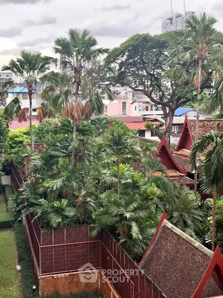Stunning view of lush tropical garden with traditional architecture and city skyline backdrop.