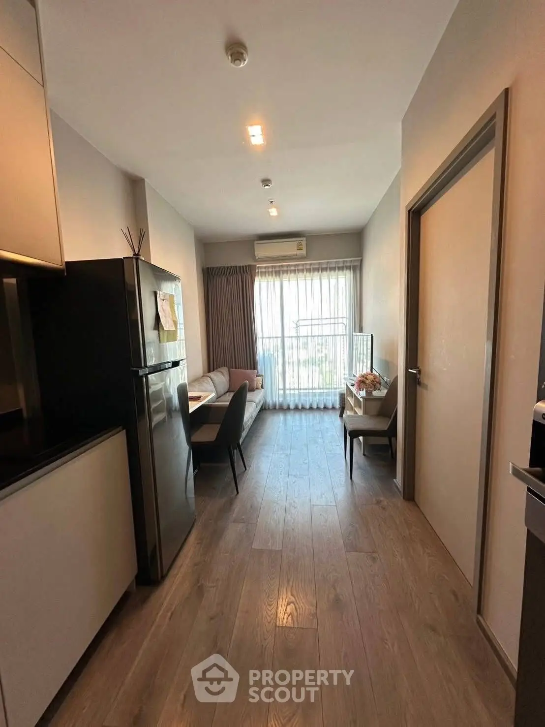 Modern apartment interior with sleek kitchen and cozy living area, featuring large window for natural light.