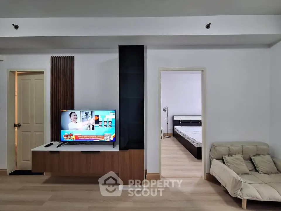 Modern living room with TV and cozy seating, adjacent to a minimalist bedroom.