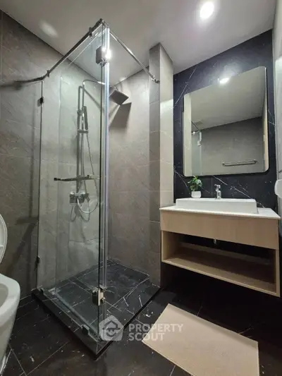 Modern bathroom with glass shower enclosure and sleek vanity in contemporary apartment.