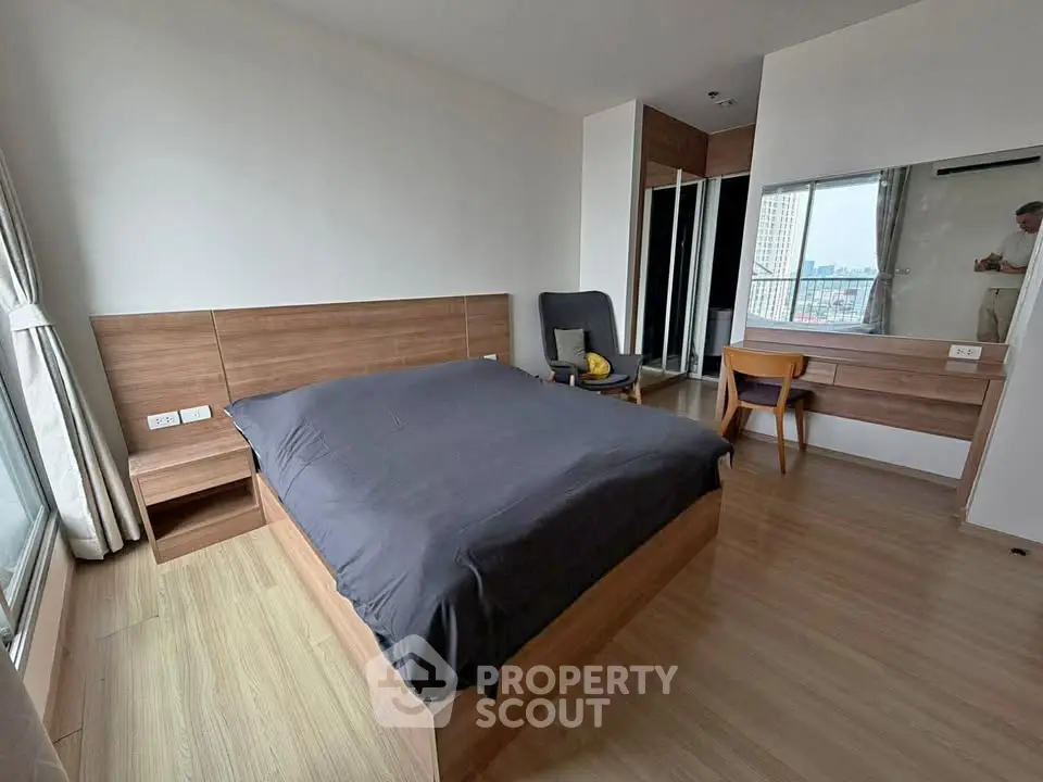 Spacious modern bedroom with wooden flooring and large window offering city views.