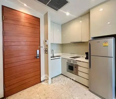 Modern kitchen with sleek cabinetry, stainless steel fridge, and built-in microwave in a compact layout.