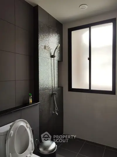 Modern bathroom with sleek black tiles and frosted window for privacy.