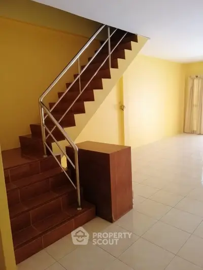 Spacious interior with tiled flooring and modern staircase in a bright yellow-painted room.