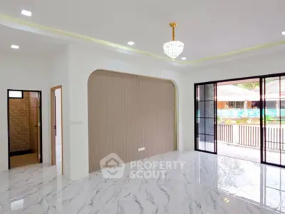 Spacious modern living room with elegant chandelier and marble flooring, featuring large sliding glass doors opening to a balcony.
