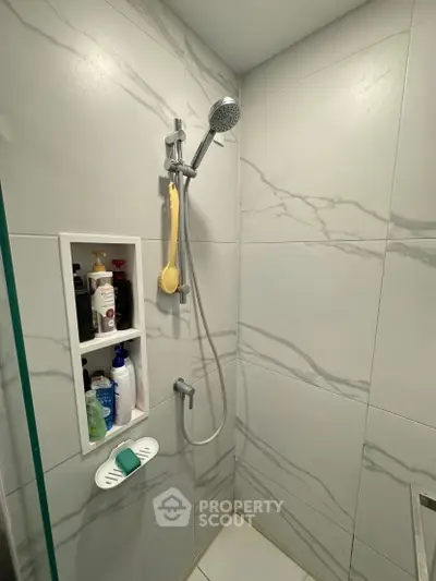 Modern bathroom shower with marble tiles and built-in shelf for toiletries.