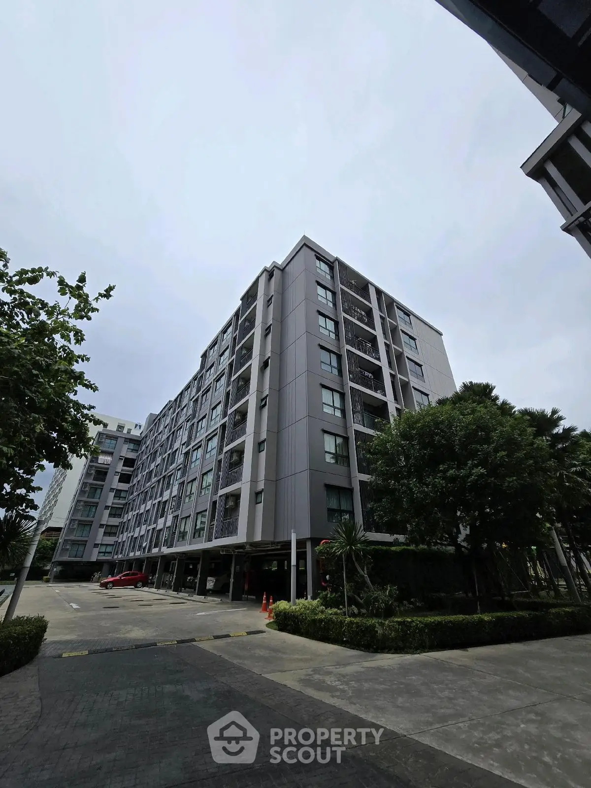 Modern residential building with lush greenery and spacious parking area.