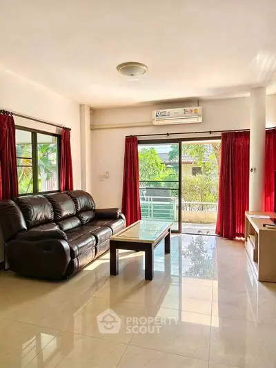 Spacious living room with leather sofa and large windows offering garden views.