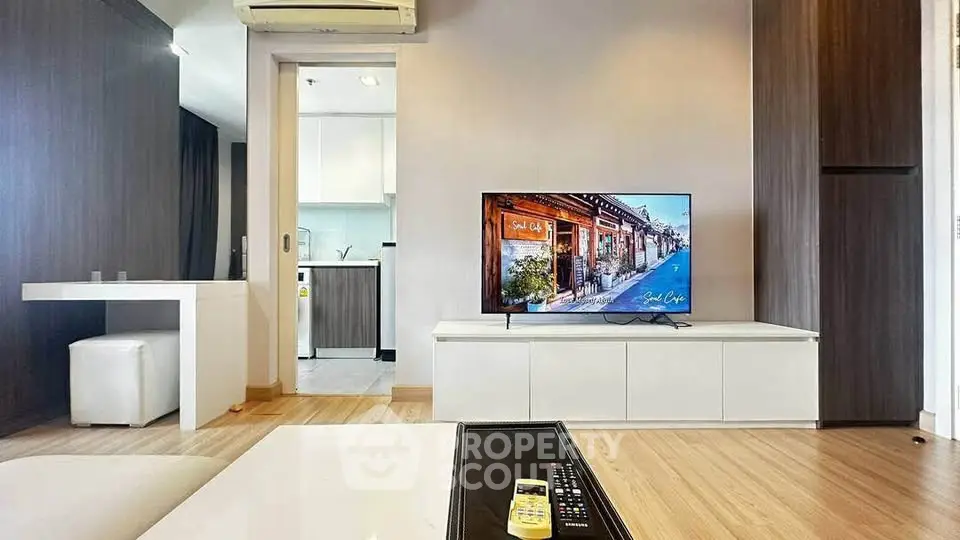 Modern living room with sleek TV setup and open kitchen layout in stylish apartment.
