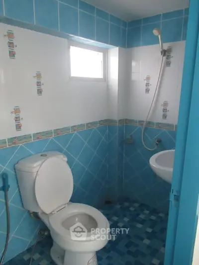 Compact bathroom with blue tiles, shower, and toilet in a cozy real estate property.