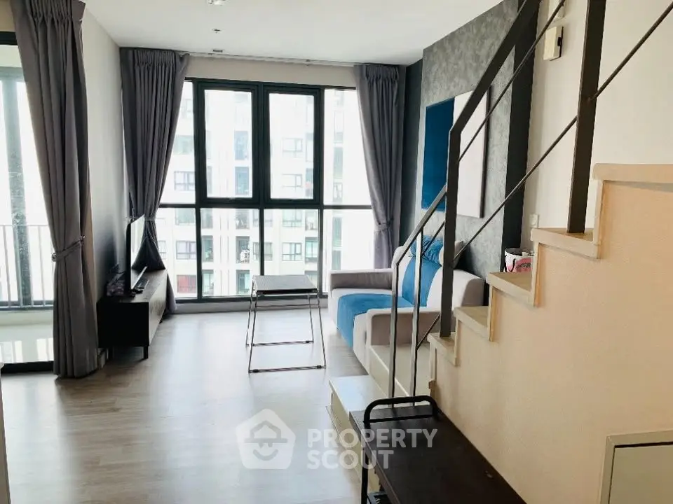 Modern living room with large windows and stylish staircase in a bright apartment.