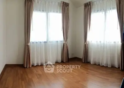Spacious empty room with wooden flooring and large windows, perfect for customization.