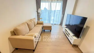 Modern living room with cozy sofa and large TV, featuring elegant wooden flooring and natural light.