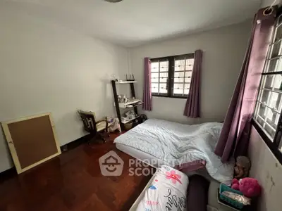 Cozy bedroom with wooden flooring and large window, featuring a comfortable bed and study desk.