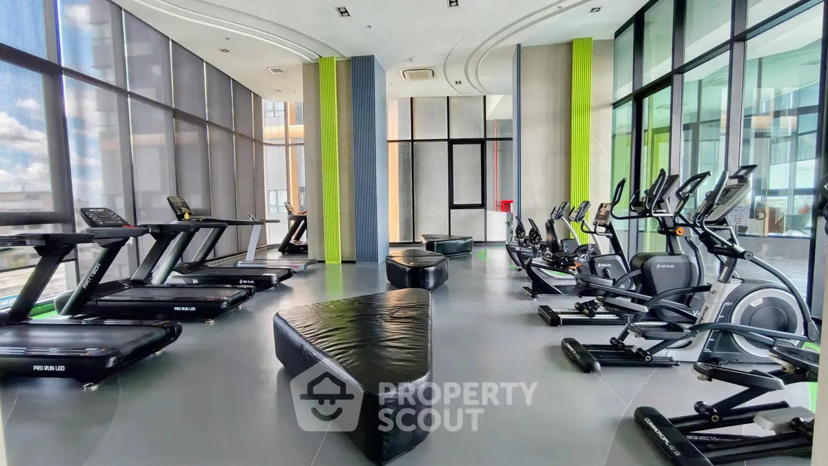 Modern gym with state-of-the-art equipment and floor-to-ceiling windows in luxury building.