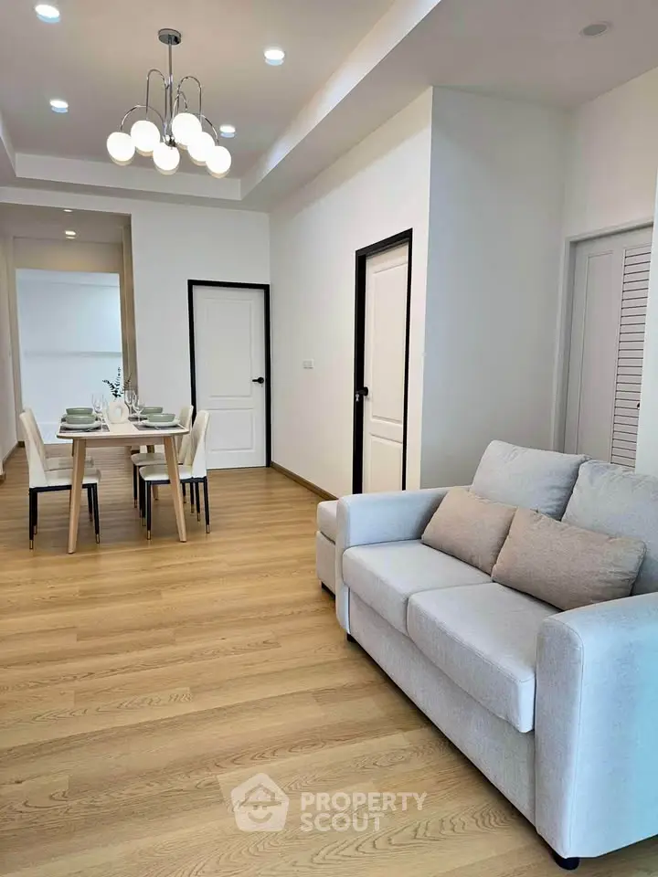 Modern living room with cozy sofa and elegant dining area, featuring stylish lighting and wooden flooring.