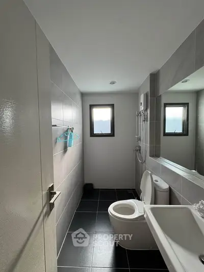 Modern bathroom with sleek design, featuring a large mirror, shower, and natural light from a window.