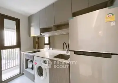 Modern kitchen with sleek cabinetry, washing machine, and large fridge in a bright, airy space.