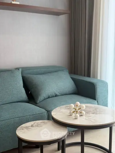 Modern living room with stylish teal sofa and elegant marble coffee tables.