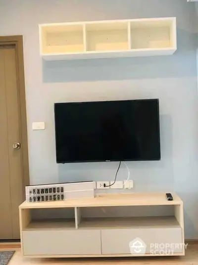 Modern minimalist living room interior with mounted flat-screen TV and sleek white storage unit, complemented by a soft blue wall for a serene ambiance.