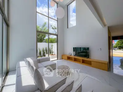 Spacious modern living room with high ceilings and large windows offering natural light and outdoor views.