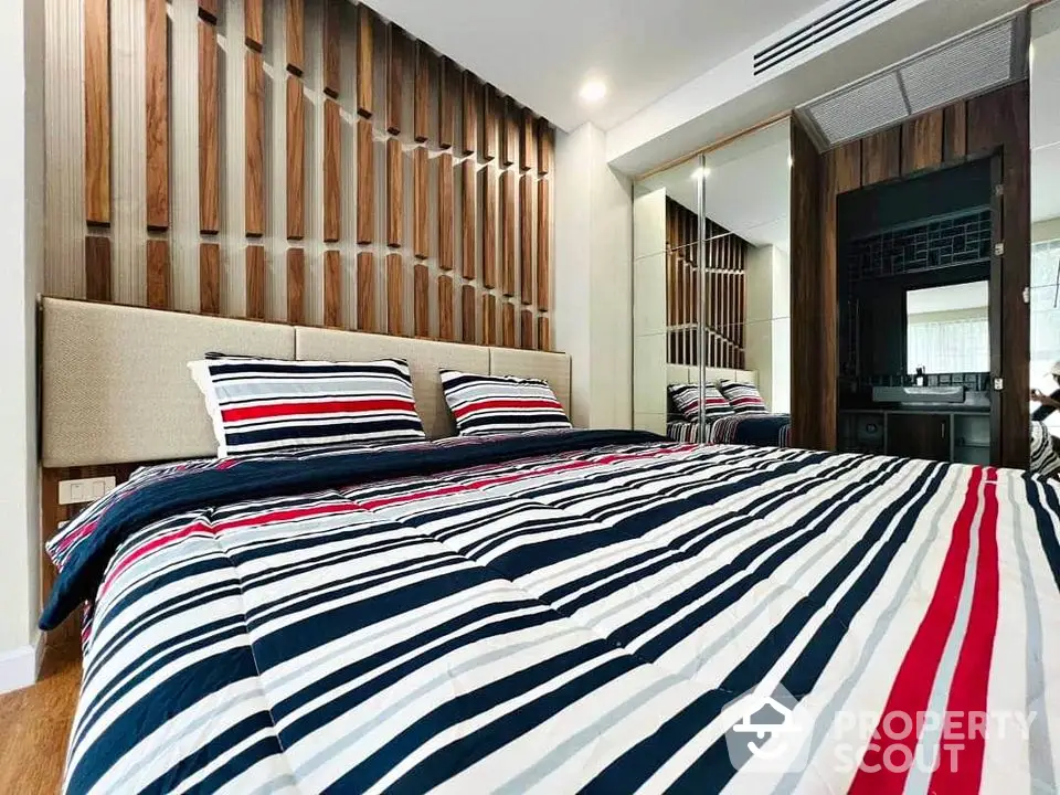 Modern bedroom with stylish wooden paneling and mirrored closet doors.