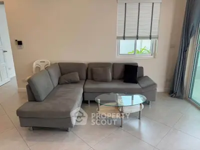 Modern living room with stylish gray sectional sofa and glass coffee table, featuring large windows for natural light.