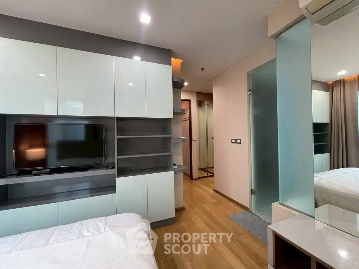 Modern bedroom with sleek built-in storage and TV, featuring wooden flooring and stylish decor.