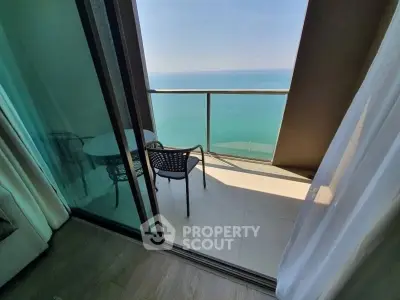 Stunning ocean view from modern balcony with glass railing and cozy seating.