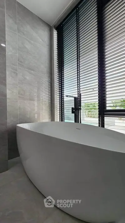 Luxurious bathroom with modern freestanding bathtub and large window with blinds.