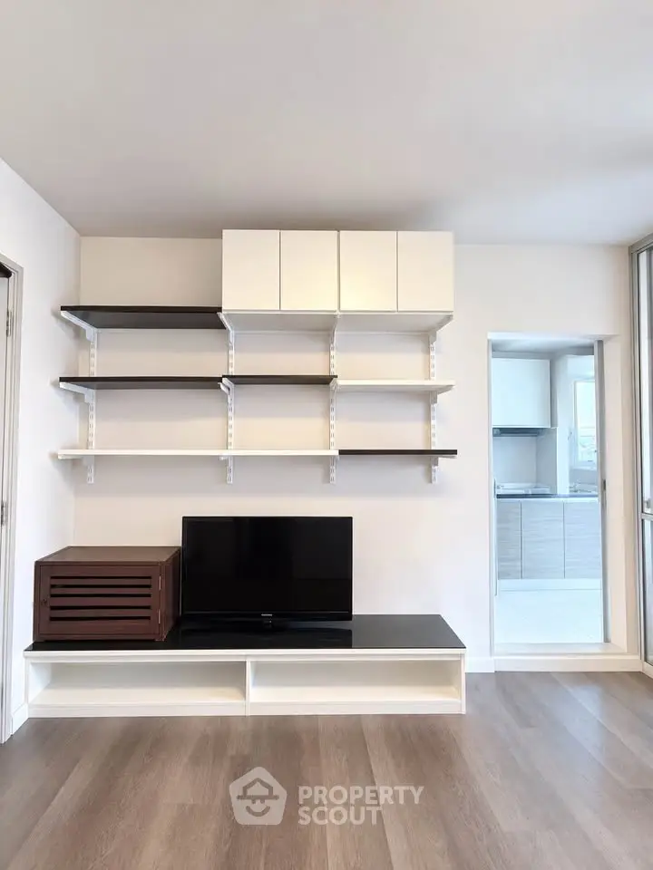 Modern living room with sleek shelving and TV setup, featuring open kitchen view.