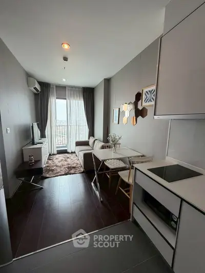 Modern living room with sleek kitchen in open layout, featuring stylish decor and large window view.