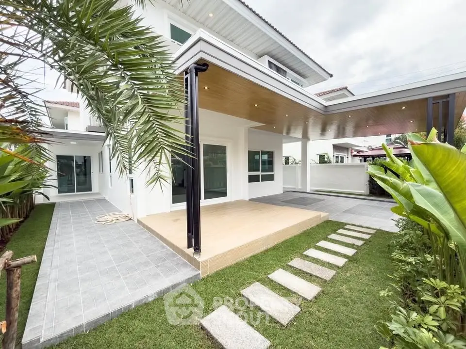 Modern white house with spacious patio and lush garden, featuring sleek architectural design and ample outdoor space.