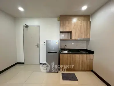 Modern kitchen with wooden cabinets and stainless steel fridge in compact apartment.
