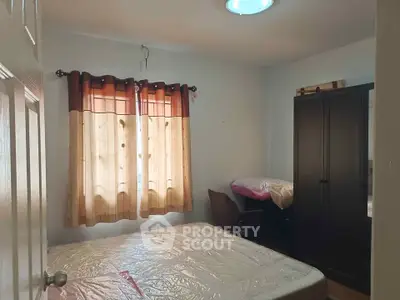 Cozy bedroom with natural light, featuring a bed, wardrobe, and window with curtains.