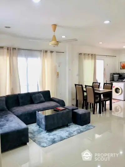 Spacious living room with modern furniture and dining area, featuring a washing machine.