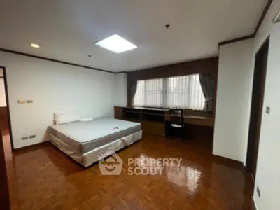 Spacious bedroom with wooden flooring and large window, featuring a comfortable bed and built-in desk.