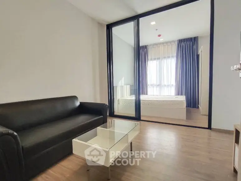 Modern apartment with glass partition separating living room and bedroom, featuring sleek furniture.