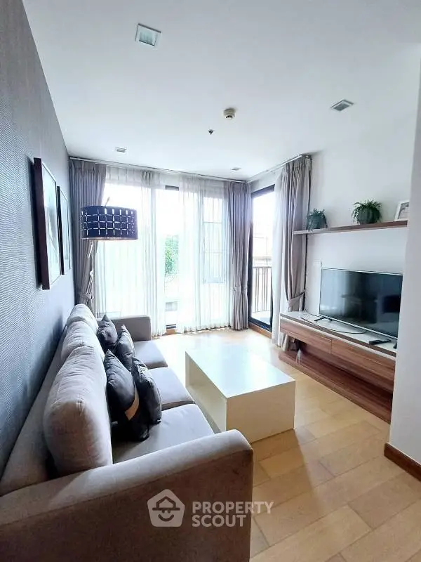 Modern living room with cozy sofa and large TV, featuring natural light from floor-to-ceiling windows.