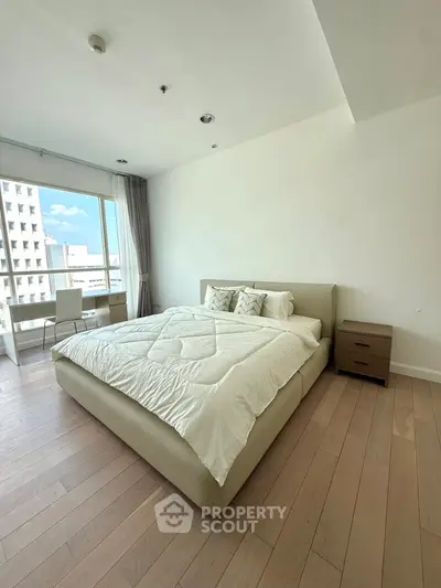 Spacious bedroom with modern decor and large window offering city views.