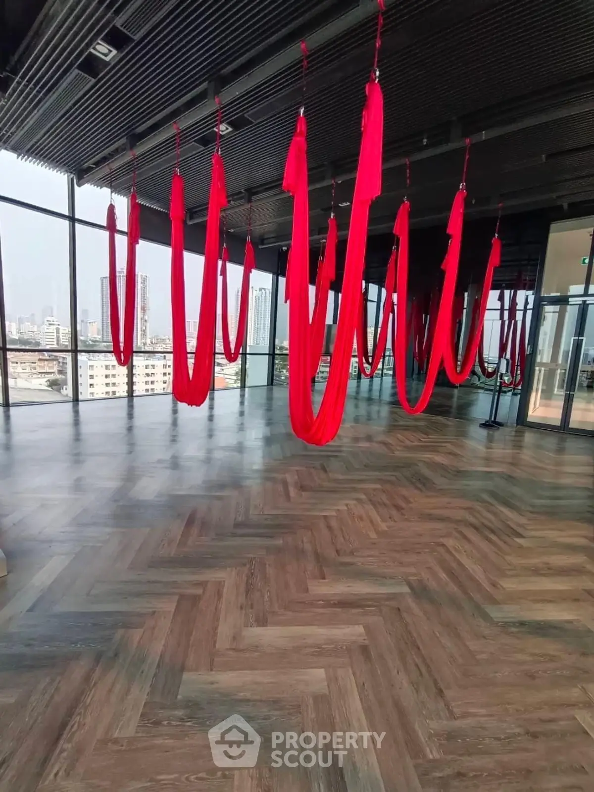 Spacious gym with aerial yoga setup and city view, perfect for fitness enthusiasts.