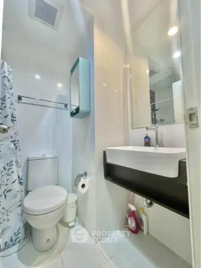 Modern bathroom with sleek fixtures and white tiles, featuring a shower curtain and under-sink storage.