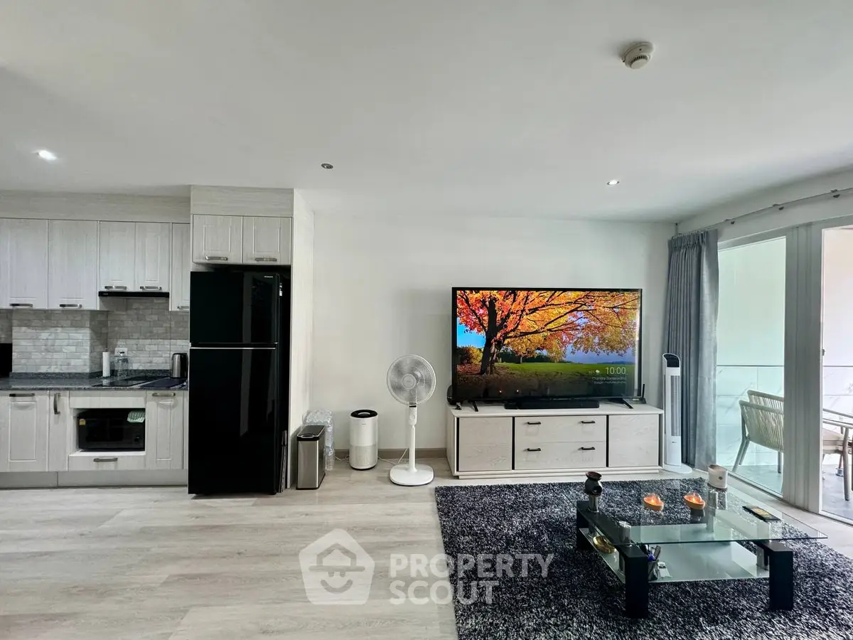 Modern open-plan living room with sleek kitchen and balcony access, featuring stylish decor and natural light.